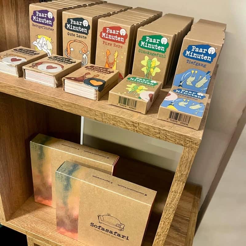 Ein Holzregal in einem lokalen Geschäft präsentiert verschiedene Paarzeit-Produkte wie die Kartenspiele PaarMinuten und Sofasafari.