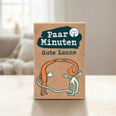 Paarzeit PaarMinuten Gute Laune Produktshot – beige Kartenbox mit dunkelblauem Logo auf Tisch mit Sofa im Hintergrund