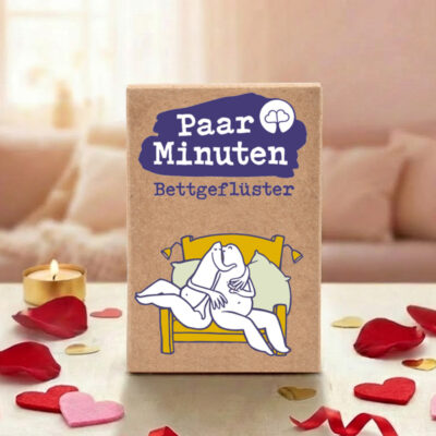Paarzeit PaarMinuten Bettgeflüster Produktshot – Kartenbox mit violettem Logo umgeben von Rosenblättern und Herzdekorationen auf weißem Untergrund zum Valentinstag