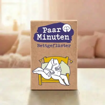 Paarzeit PaarMinuten Bettgeflüster Produktshot – Kartenbox mit violettem Logo auf Tisch mit Sofa im Hintergrund