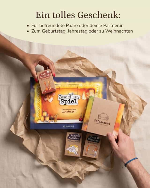 Aufsicht auf hellen Stoff mit zerknittertem Packpapier: In der Mitte liegt die farbig illustrierte Schachtel des ZusammenSpiels mit Jahrmarkt-Motiv, rechts daneben die Kraftpapier-Box der Sofasafari mit gezeichnetem Sofa, davor die beiden PaarMinuten-Schachteln Bettgeflüster und Gute Laune. Von oben links greift eine Hand mit rot lackierten Nägeln nach der Schachtel PaarMinuten Fürs Herz, von rechts kommt eine zweite Hand mit blauem Armband ins Bild. Eingeblendet: „Ein tolles Geschenk: Für befreundete Paare oder dein:e Partner:in. Zum Geburtstag, Jahrestag oder zu Weihnachten.“