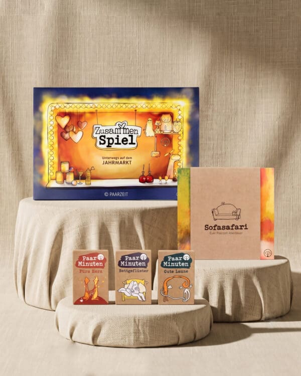 Fünf Paarzeit-Produkte auf beigefarbenen Leinenpodesten vor Leinenhintergrund: der Spielkarton ZusammenSpiel, das Sofasafari-Heft und die drei Kartensets PaarMinuten Fürs Herz, Bettgeflüster und Gute Laune