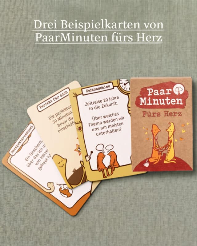 Die Schachtel PaarMinuten Fürs Herz liegt auf graugrünem Leinen, davor drei aufgefächerte Fragekarten der Kategorien Perspektivwechsel, Perfekt für dich und Zeitmaschine