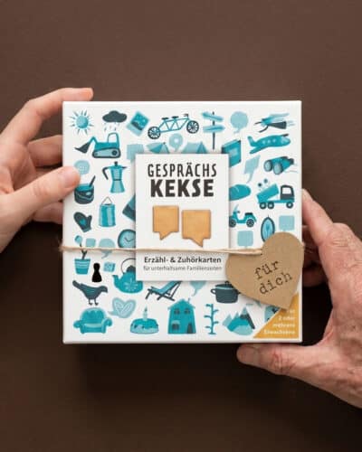 Zwei Hände halten die Schachtel Gesprächskekse mit türkisen Illustrationen, am Verschluss hängt ein Kraftpapier-Herz mit der Aufschrift für dich