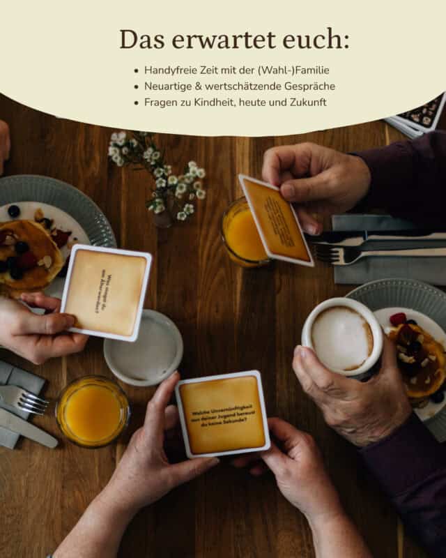 Blick von oben auf einen gedeckten Frühstückstisch mit Pancakes, Kaffee und Orangensaft; vier Hände unterschiedlichen Alters halten keksförmige Fragekarten