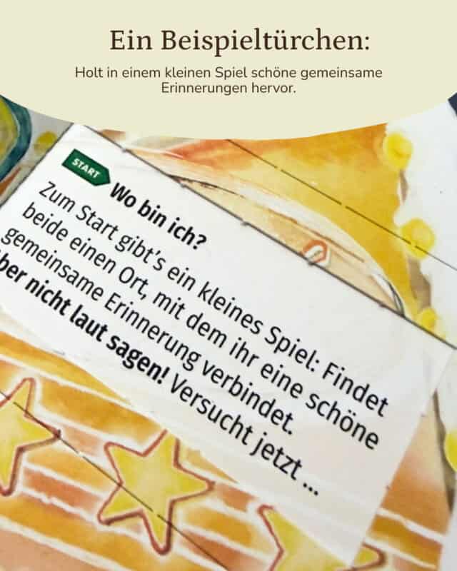 Nahaufnahme eines geöffneten Türchens des PaarMinuten Adventskalenders 2026 auf gelb-orange illustriertem Untergrund mit gemalten Sternen; auf dem Zettel steht „Start – Wo bin ich? Zum Start gibt’s ein kleines Spiel: Findet beide einen Ort, mit dem ihr eine schöne gemeinsame Erinnerung verbindet. Versucht jetzt … aber nicht laut sagen!“ Eingeblendet: „Ein Beispieltürchen: Holt in einem kleinen Spiel schöne gemeinsame Erinnerungen hervor.“
