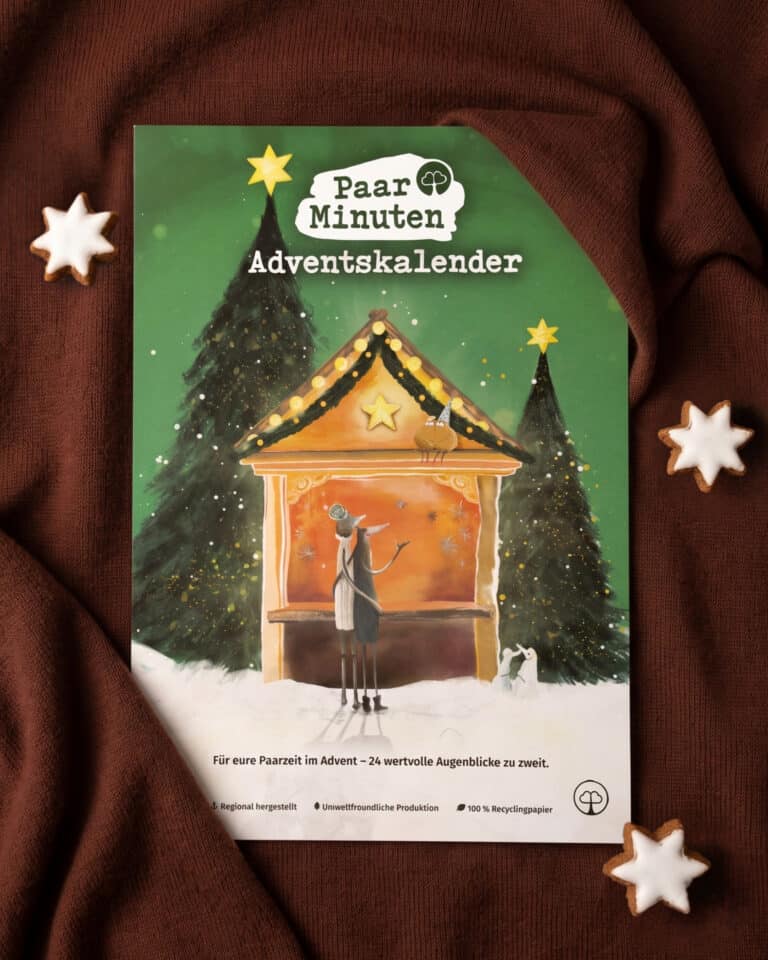 Der grüne PaarMinuten Adventskalender 2026 liegt auf braunem Strickstoff zwischen Zimtsternen; die Illustration zeigt ein Paar vor einer beleuchteten Weihnachtsmarktbude zwischen verschneiten Tannen, darunter „Für eure Paarzeit im Advent – 24 wertvolle Augenblicke zu zweit“.