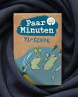 Schachtel PaarMinuten Tiefgang auf dunkelblau drapiertem Stoff, die Illustration zeigt zwei tauchende Robben