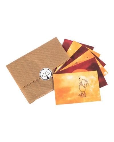 Vor weißem Hintergrund liegt eine flache braune Kraftpapiertüte mit gezacktem Rand, verschlossen mit einem runden weißen Aufkleber mit dem Paarzeit-Logo, einem Baum mit zwei Herzen als Krone. Rechts daneben sind sechs kleine Postkarten fächerförmig ausgelegt, alle in warmen Aquarelltönen von Gelb über Orange bis Dunkelrot; die vorderste Karte zeigt eine gezeichnete Figur mit langen Ohren und Turnschuhen, die etwas in den Händen hält, darüber ein kleines Herz.