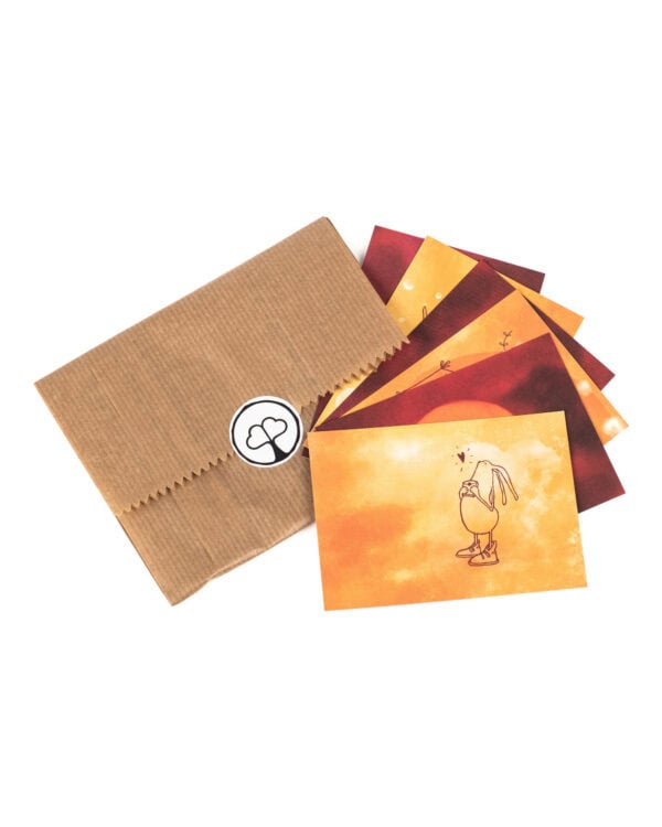 Vor weißem Hintergrund liegt eine flache braune Kraftpapiertüte mit gezacktem Rand, verschlossen mit einem runden weißen Aufkleber mit dem Paarzeit-Logo, einem Baum mit zwei Herzen als Krone. Rechts daneben sind sechs kleine Postkarten fächerförmig ausgelegt, alle in warmen Aquarelltönen von Gelb über Orange bis Dunkelrot; die vorderste Karte zeigt eine gezeichnete Figur mit langen Ohren und Turnschuhen, die etwas in den Händen hält, darüber ein kleines Herz.