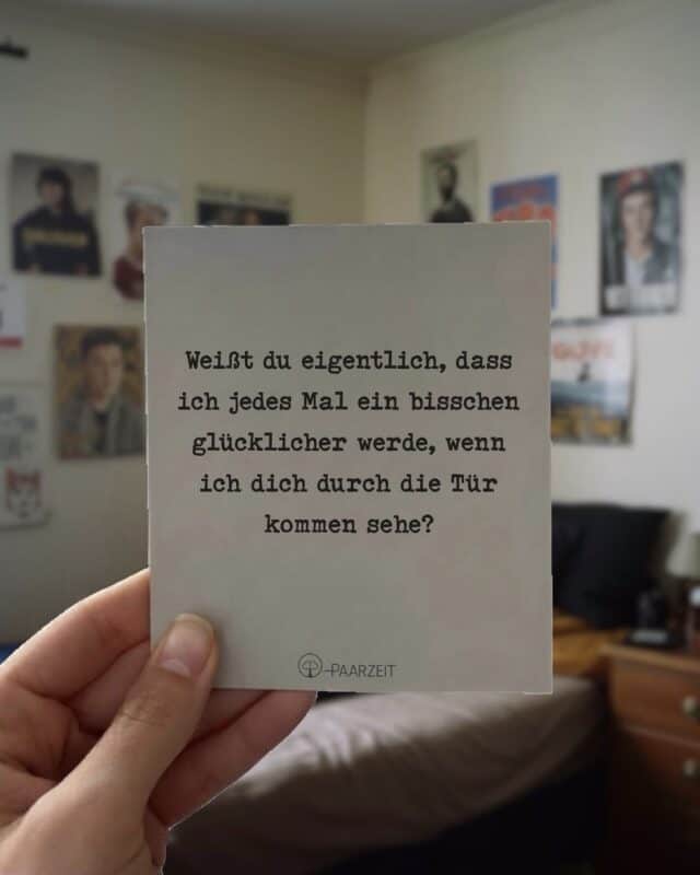 Eine Hand hält eine quadratische Paarzeit-Karte mit dem Spruch: „Weißt du eigentlich, dass ich jedes Mal ein bisschen glücklicher werde, wenn ich dich durch die Tür kommen sehe?“