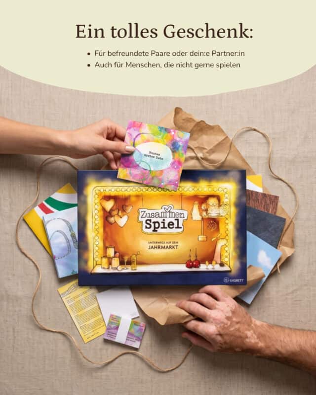 Der Spielkarton „ZusammenSpiel – Unterwegs auf dem Jahrmarkt“ liegt mit den Rätselumschlägen und Hilfekarten auf Kraftpapier; zwei Hände greifen von links und rechts ins Bild
