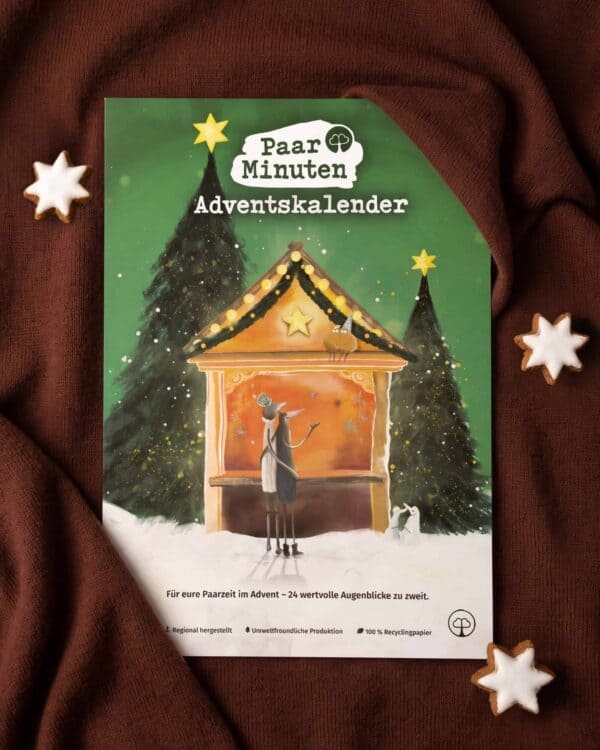 Der grüne PaarMinuten Adventskalender 2026 liegt auf braunem Strickstoff zwischen Zimtsternen; die Illustration zeigt ein Paar vor einer beleuchteten Weihnachtsmarktbude zwischen verschneiten Tannen, darunter „Für eure Paarzeit im Advent – 24 wertvolle Augenblicke zu zweit“.