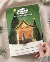 Eine Hand hält den grünen PaarMinuten Adventskalender 2026 schräg über einer hellen Leinendecke, daneben liegen Tannenzweige, im Hintergrund warme Lichtpunkte. Die Illustration zeigt eine beleuchtete Weihnachtsmarktbude zwischen verschneiten Tannen, darunter steht „Für eure Paarzeit im Advent – 24 wertvolle Augenblicke zu zweit“ und in kleiner Schrift „Regional hergestellt“, „Umweltfreundliche Produktion“ und „100 % Recyclingpapier“.