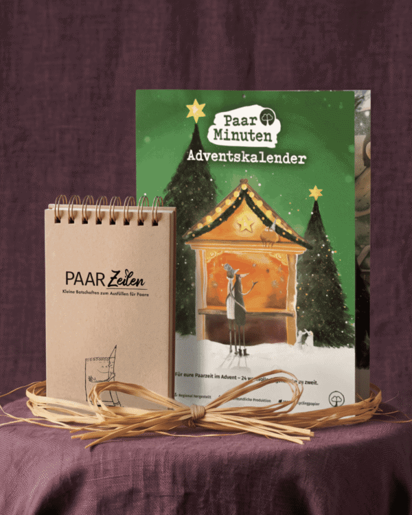 Der grüne PaarMinuten Adventskalender 2026 steht auf einem runden Tisch mit violettem Leinentuch vor violettem Stoff. Die Illustration zeigt zwei Figuren vor einer beleuchteten Weihnachtsmarktbude zwischen verschneiten Tannen, darunter „Für eure Paarzeit im Advent – 24 wertvolle Augenblicke zu zweit“. Davor steht der Block PaarZeilen mit Kraftpapier-Deckel, goldener Spiralbindung und der Aufschrift „PAAR Zeilen – Kleine Botschaften zum Ausfüllen für Paare“; um beide liegt eine Schleife aus Bast.